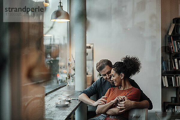 Lächelnde Frau lehnt sich an einen Mann  während sie im Café sitzt