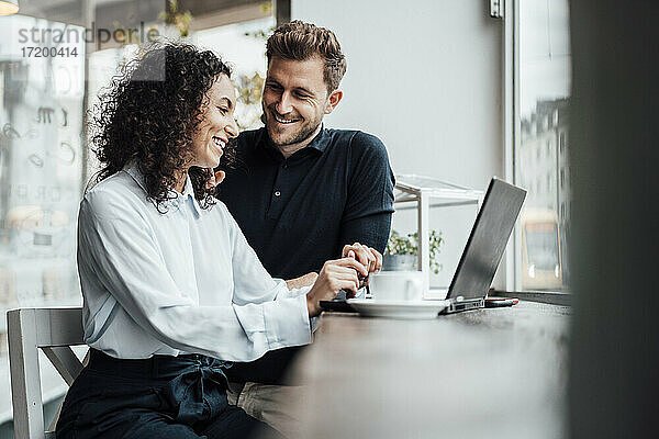 Junge Geschäftsfrau arbeitet am Laptop  während sie neben einem Kollegen im Café sitzt