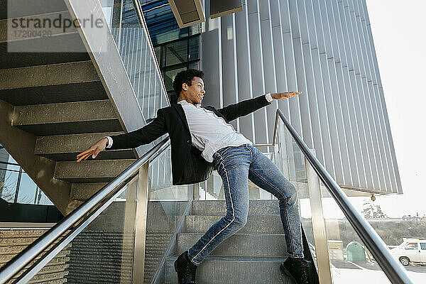 Männlicher Tänzer mit ausgestreckten Armen tanzt  während er sich auf ein Treppengeländer stützt