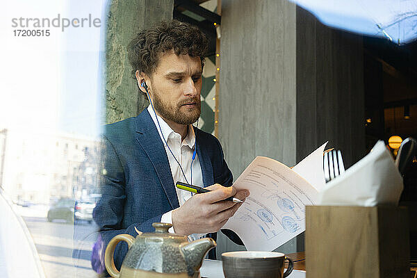 Geschäftsmann mit In-Ear-Kopfhörern  der in einem Café sitzt und seine Strategie überprüft