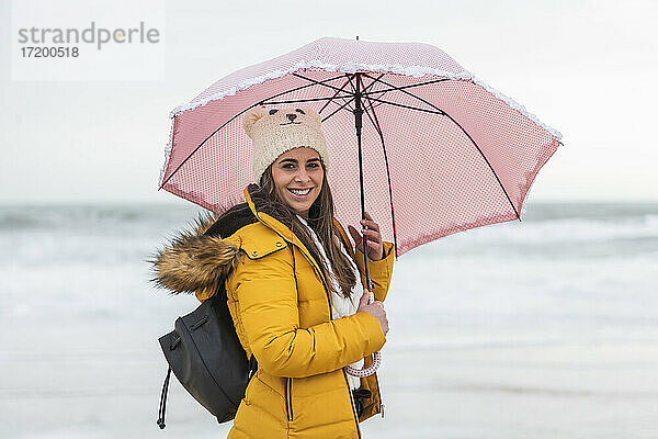 Porträt einer jungen Frau am Strand mit Regenschirm in den Händen