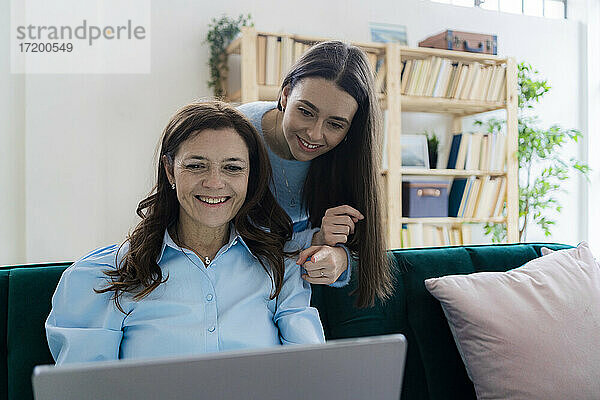 Lächelnde Geschäftsfrau und Tochter  die im Heimbüro auf einen Laptop schauen