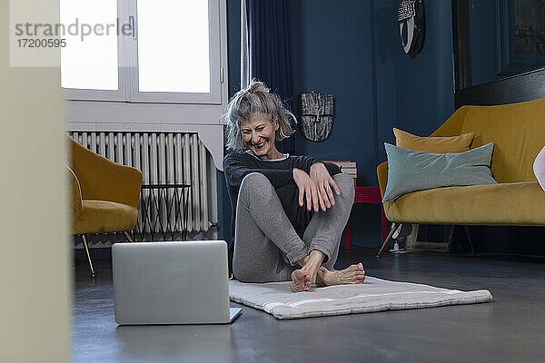 Lächelnde ältere Frau  die zu Hause sitzend ein Tutorial auf dem Laptop anschaut