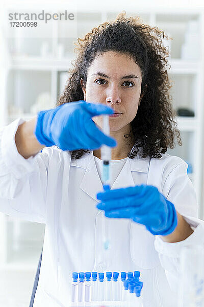 Ärztin beim Mischen einer Lösung im Reagenzglas durch eine Spritze im Chemielabor