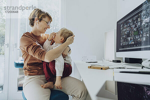 Liebevolle Mutter  die ihren Sohn umarmt  der auf ihrem Schoß im Büro sitzt
