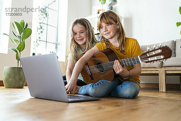 Lächelnde Mädchen e-learning Gitarren-Tutorial durch Laptop im Wohnzimmer zu Hause