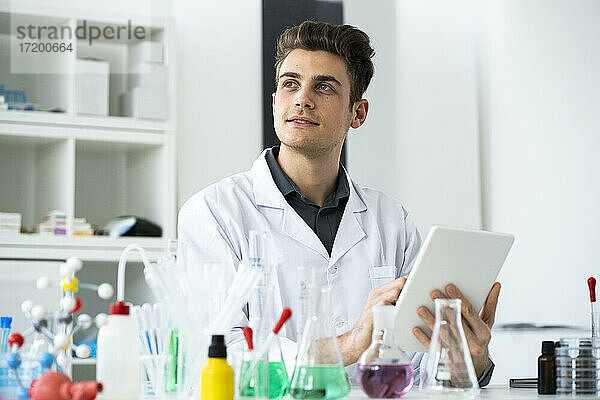 Nachdenklicher männlicher Wissenschaftler  der ein digitales Tablet benutzt  während er im Labor wegschaut