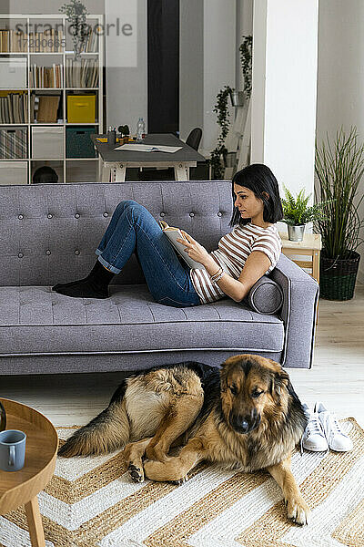 Junge Frau liest ein Buch  während der Hund zu Hause auf dem Teppich sitzt