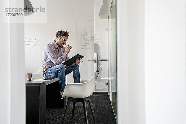 Geschäftsmann beim Brainstorming mit Blick auf das Klemmbrett im Büro
