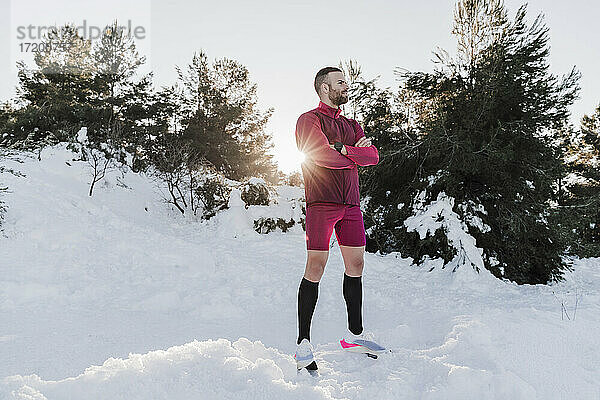 Sportler mit verschränkten Armen steht auf schneebedecktem Land gegen klaren Himmel