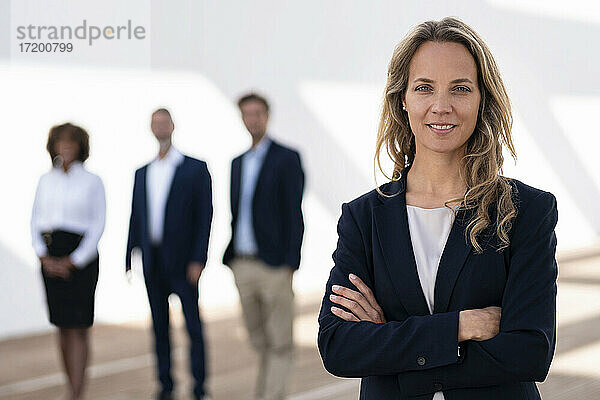 Mittlere erwachsene Geschäftsfrau stehend mit Kollegen im Hintergrund auf einer Büroterrasse