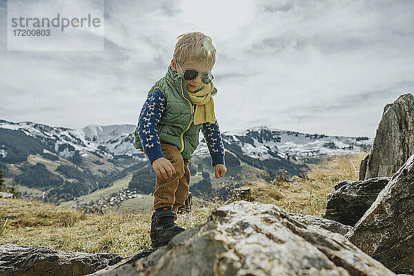 Junge mit Sonnenbrille beim Klettern auf einem Felsen gegen den Himmel im Salzburger Land  Leoganger Berge  Österreich