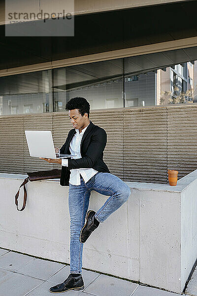 Mittlerer erwachsener Geschäftsmann  der auf einem Bein steht und einen Laptop benutzt