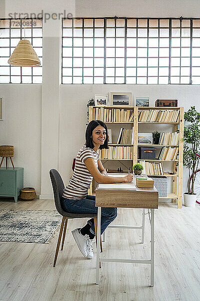 Frau sitzt auf einem Stuhl am Tisch vor einem Bücherregal im Wohnzimmer