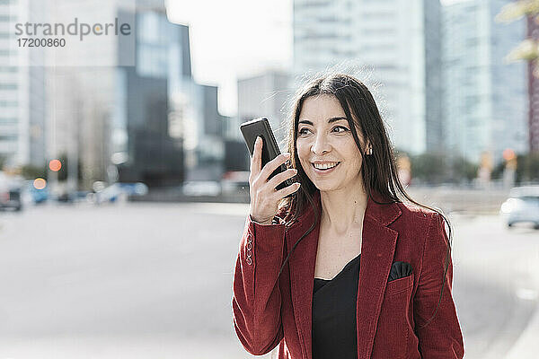 Lächelnde Geschäftsfrau  die in der Stadt mit einem Smartphone telefoniert