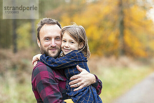 Lächelnde Tochter umarmt Vater im Wald stehend