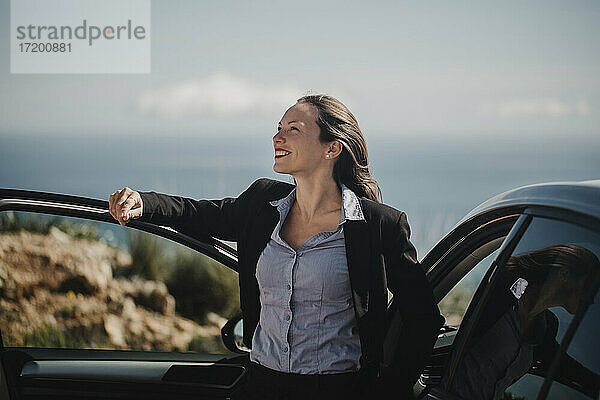 Lächelnde Geschäftsfrau träumt  während sie am Auto steht
