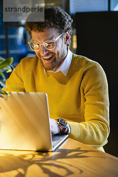 Lachender männlicher Besitzer  der in einem Café am Laptop arbeitet