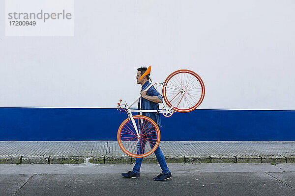 Mann trägt Fahrrad  während er auf der Straße geht