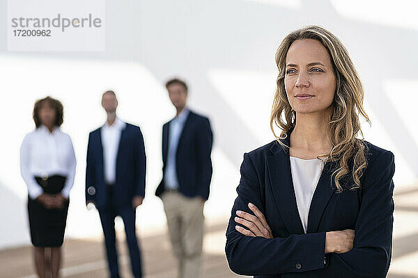 Weibliche Unternehmerin schaut weg  während sie mit Kollegen im Hintergrund auf einer Büroterrasse steht