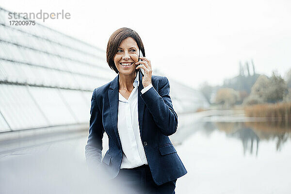 Lächelnde Geschäftsfrau  die außerhalb des Büros mit einem Smartphone spricht