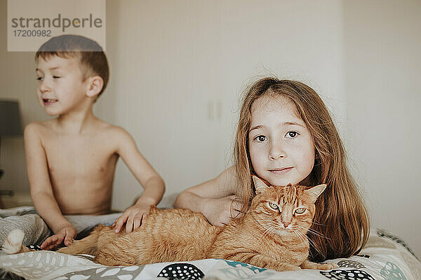 Mädchen lehnt sich an eine Katze  während ihr Bruder im Schlafzimmer wegschaut