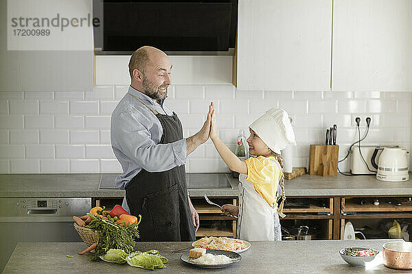 Reife Männer und Mädchen jubeln mit High-Five  während sie in der Küche zu Hause stehen