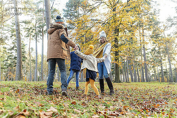 Verspielte Eltern und Kinder halten sich beim Spielen im Wald an den Händen