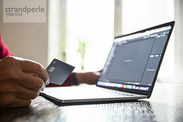 Älterer Mann kauft zu Hause mit Laptop und Kreditkarte online ein