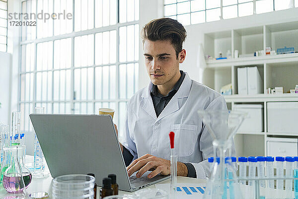 Seriöser männlicher Wissenschaftler  der an einem Laptop arbeitet  während er am Schreibtisch in einem Labor sitzt