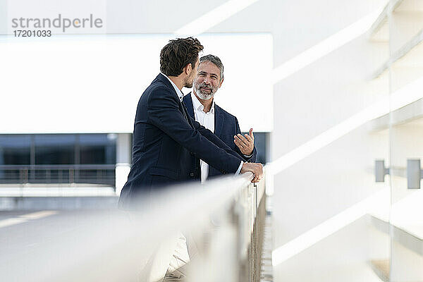 Älterer Geschäftsmann lächelt im Gespräch mit einem Kollegen auf der Terrasse eines Bürogebäudes