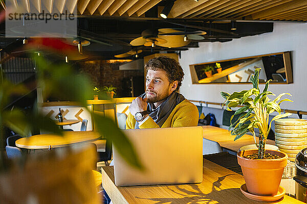 Nachdenklicher männlicher Besitzer mit Laptop  der wegschaut  während er im Café sitzt