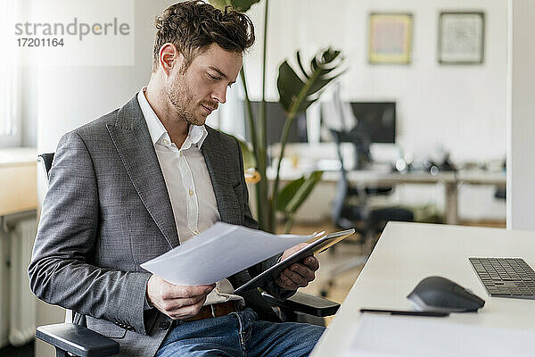 Männlicher Unternehmer bei der Arbeit an einem Dokument und einem digitalen Tablet im Büro