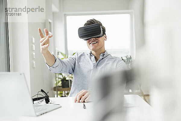 Junger Geschäftsmann gestikuliert  während er einen Virtual-Reality-Simulator im Büro zu Hause trägt