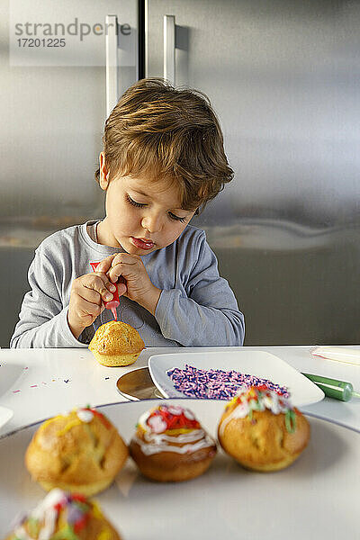 Süßer Junge dekoriert Muffin am Küchentisch