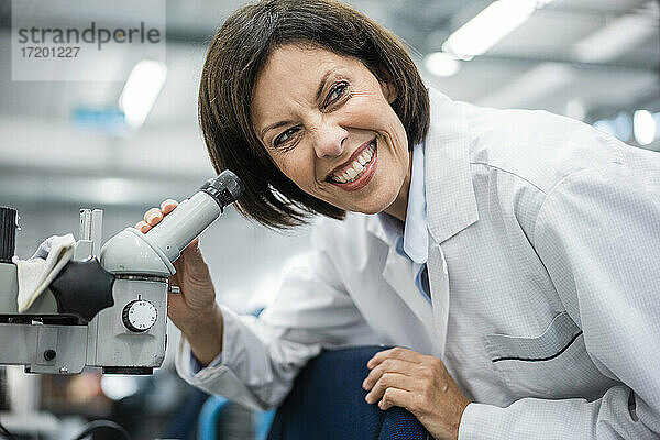 Lächelnde Wissenschaftlerin mit Mikroskop im Labor
