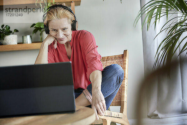 Frau mit Kopfhörern bei einem Videogespräch auf dem Laptop zu Hause