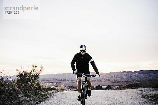 Männlicher Radfahrer fährt Fahrrad gegen den Himmel bei Sonnenuntergang