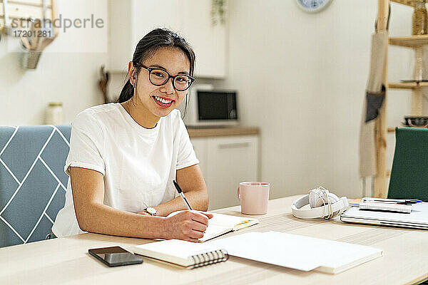 Lächelnde Frau mit Brille sitzt zu Hause bei einem Buch