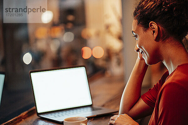 Lächelnde Frau arbeitet am Laptop  während sie im Café sitzt