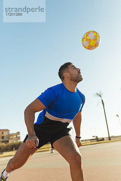 Mann köpft Ball beim Fußballspielen an einem sonnigen Tag