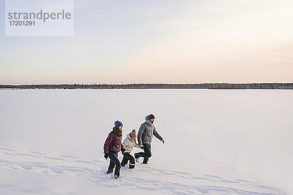 Familie  die sich an den Händen hält  während sie im Winter auf Schnee gegen den Himmel läuft