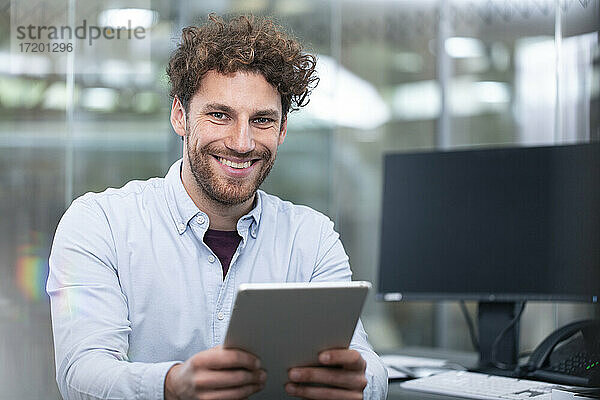 Lächelnder männlicher Unternehmer mit digitalem Tablet im Büro