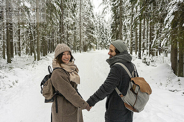 Junge Frau lächelt  während sie die Hand eines im Wald stehenden Mannes hält