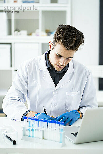 Junge Wissenschaftlerin schreibt Notizen  während sie am Schreibtisch im Labor sitzt