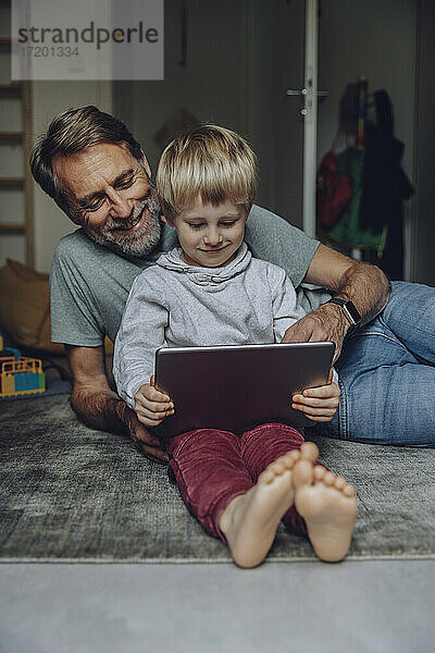 Lächelnder Vater beobachtet seinen Sohn bei der Nutzung eines Tablets im Schlafzimmer