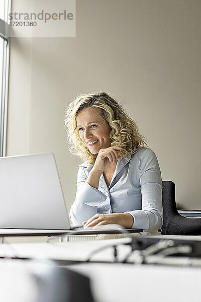 Lächelnde Unternehmerin  die im Büro sitzend einen Laptop betrachtet