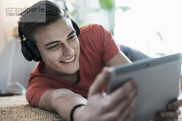 Lächelnder junger Mann mit drahtlosen Kopfhörern  der ein Video auf einem digitalen Tablet anschaut