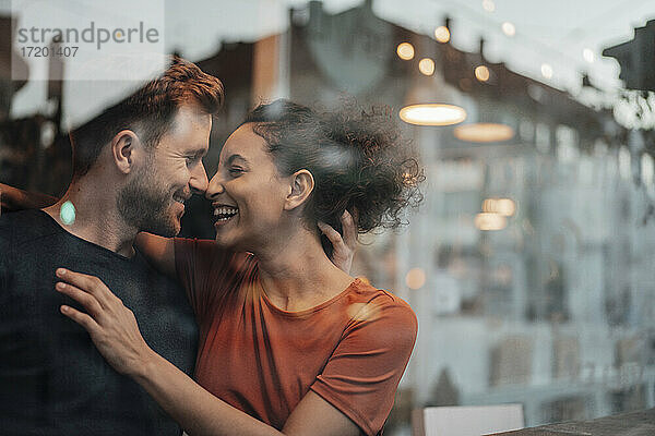 Lächelndes Paar  das sich die Nasen reibt  während es am Fenster eines Cafés sitzt