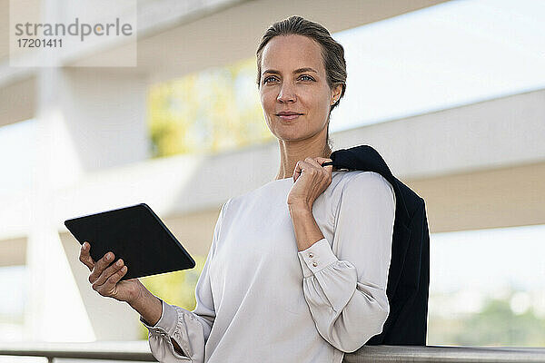 Unternehmerin mit digitalem Tablet und Jacke auf der Büroterrasse